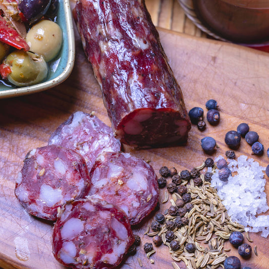 Good Game Salami whole piece and slices on a wooden board with juniper, fennel and pepper